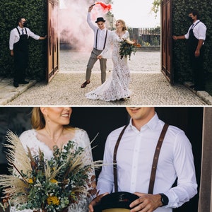 May include: A wedding couple stands together, one in a long-sleeved white lace gown and the other in a white button-down shirt with brown leather suspenders, grey trousers, and a black hat, holding a large bouquet of dried flowers and pampas grass.