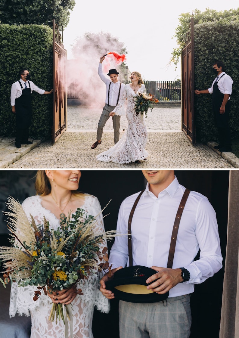 May include: A wedding couple stands together, one in a long-sleeved white lace gown and the other in a white button-down shirt with brown leather suspenders, grey trousers, and a black hat, holding a large bouquet of dried flowers and pampas grass.