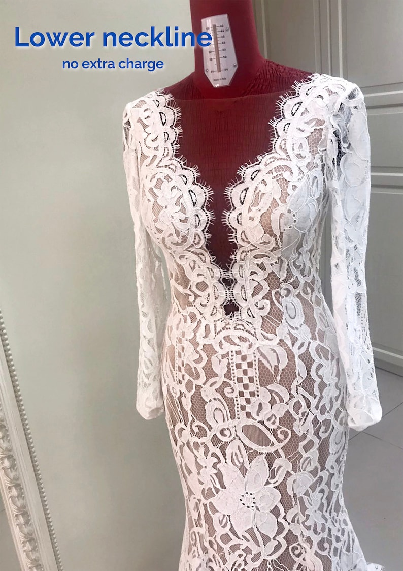 May include: A white long-sleeved lace dress with a deep V-neckline and a nude-colored lining. The dress features intricate floral lace patterns and scalloped edges along the neckline. Text on the image reads: Lower neckline no extra charge.