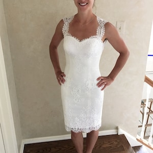 Puede incluir: Un vestido blanco de encaje con escote de coraz&oacute;n y tirantes finos. El vestido es ajustado y tiene un largo hasta la rodilla.