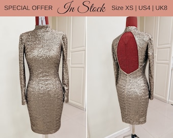 May include: A gold sequined dress with long sleeves and a low back. The dress has a fitted silhouette and is shown on a mannequin. The text "In Stock" and "Size XS | US4 | UK8" is displayed above the dress.