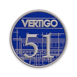 May include: A circular embroidered patch with a royal blue background and a silver-grey border. The word VERTIGO is stitched in silver-grey above the large number 51, which is also in silver-grey, set against a grid of thin silver-grey lines.