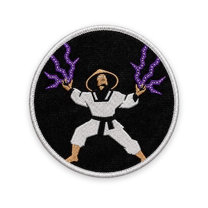 Peut inclure: Un écusson brodé circulaire sur fond noir représentant une silhouette en uniforme d'arts martiaux blanc et chapeau beige. La silhouette a les bras levés, avec des éclairs violets émanant de chaque main. L'écusson a une bordure cousue blanche.