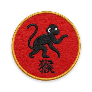 May include: A circular embroidered patch featuring a red background with a gold border. In the center, a black monkey silhouette is depicted with a white eye. Below the monkey, the black Chinese character for monkey, 猴, is stitched.