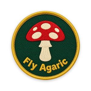 Puede incluir: Un parche bordado circular con un fondo verde oscuro y un hongo rojo y blanco en el centro. El texto Fly Agaric está bordado en letras amarillas en la parte inferior. El parche tiene un borde amarillo grueso alrededor del contorno.