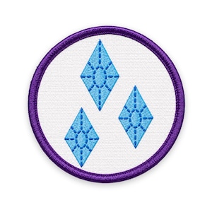 May include: A circular embroidered patch featuring a white background with a thick purple border. The center displays three light blue diamond-shaped icons, each detailed with a stitched oval pattern in the middle and vertical lines.