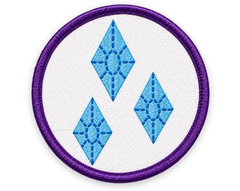 May include: A circular embroidered patch featuring a white background with a thick purple border. The center displays three light blue diamond-shaped icons, each detailed with a stitched oval pattern in the middle and vertical lines.