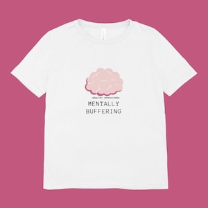 May include: White t-shirt featuring a pink cloud graphic with the words "MENTALLY BUFFERING" in black font. Above the text is the phrase "MODALITA' SOPRAVVIVENZA" in a smaller font. The shirt has short sleeves and a crew neck.