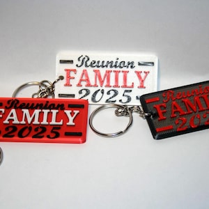 Könnte beinhalten: Drei rechteckige Schlüsselanhänger mit dem Text "Reunion FAMILY 2025". Einer ist rot mit weißem Text, einer ist weiß mit rotem Text und einer ist schwarz mit rotem Text. Jeder Schlüsselanhänger hat einen silbernen Schlüsselring.