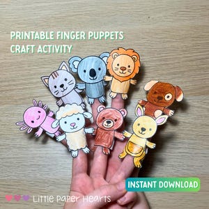 May include: A hand displays colorful printable finger puppets of various animals, including a cat, koala, lion, dog, axolotl, sheep, bear, and kangaroo. The puppets are designed for a craft activity, with the text "PRINTABLE FINGER PUPPETS CRAFT ACTIVITY" at the top.