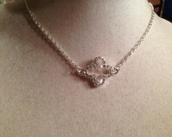 May include: A silver chain necklace with a four-leaf clover pendant. The pendant is made of silver and has clear rhinestones around the edges.