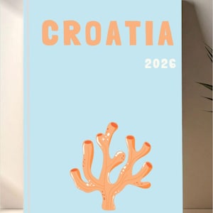 Puede incluir: Un cuaderno azul claro con la palabra "CROATIA" en letras naranjas y el año "2026" en blanco. Una ilustración de coral naranja está en la parte inferior. El cuaderno se muestra sobre una superficie blanca.