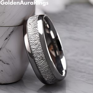 May include: A close-up of a silver ring with a textured, patterned band. The ring has a polished, shiny finish and is set against a blurred background. The brand name "Golden Aura Rings" is visible in the top left corner.