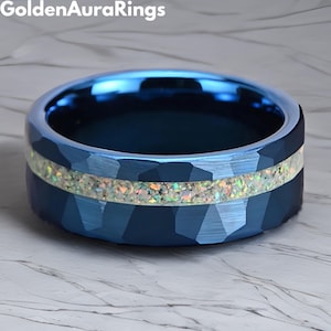 May include: A blue ring with a textured surface and a band of iridescent material. The ring is a close-up shot, showcasing the details of the design. The ring is from Golden Aura Rings.