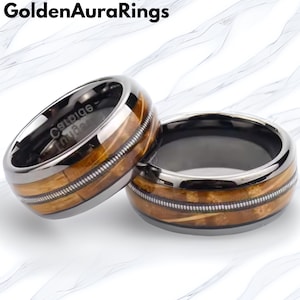 May include: Two rings with a silver band and a dark interior. The rings feature a wood-grain pattern in the centre, with a thin silver line running through the wood. The rings are from Golden Aura Rings.