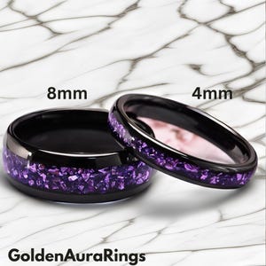 May include: Two black rings with a band of crushed purple stones. One ring is 8mm wide, the other is 4mm wide. The rings are set against a white and gray marble background. The text "GoldenAuraRings" is at the bottom.