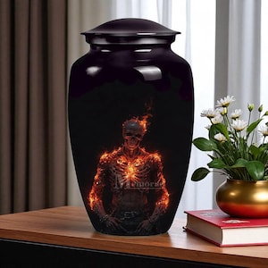 Könnte beinhalten: Schwarze Urne mit glänzendem Finish. Die Urne zeigt eine Illustration eines Skeletts, das von Flammen verschlungen wird. Das Wort "Memories" ist auf der Urne zu sehen. Die Urne hat einen passenden Deckel.