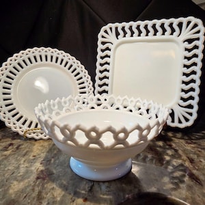 May include: A set of three white milk glass pieces including a round plate, a square plate, and a footed bowl. Each piece features an intricate openwork lattice border design with a repeating pattern along the edges of the white glass surfaces.