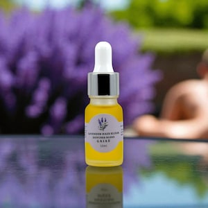 Puede incluir: Una pequeña botella de vidrio amarillo de Lavender Haze Elixir Diffuser Blend. La botella tiene una tapa cuentagotas blanca y un collar plateado. La etiqueta presenta una ilustración de una ramita de lavanda y el texto "GAIAE 10ml".