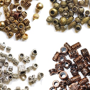 Può includere: Assortimento di perline metalliche in quattro colori diversi: oro, argento, rame e bronzo. Le perline sono di varie forme e dimensioni, alcune con disegni intricati.