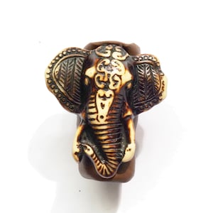 May include: A brown and white elephant head carved from wood. The elephant has intricate details and is a decorative piece.