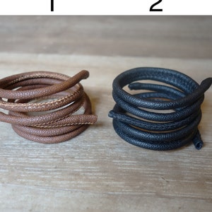 May include: Two spools of leather cord, one brown and one black. The cords are coiled and have a textured surface.