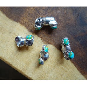 May include: Four silver rings with turquoise stones. The rings are all different designs, but they all have a similar style. The rings are on a wooden surface.
