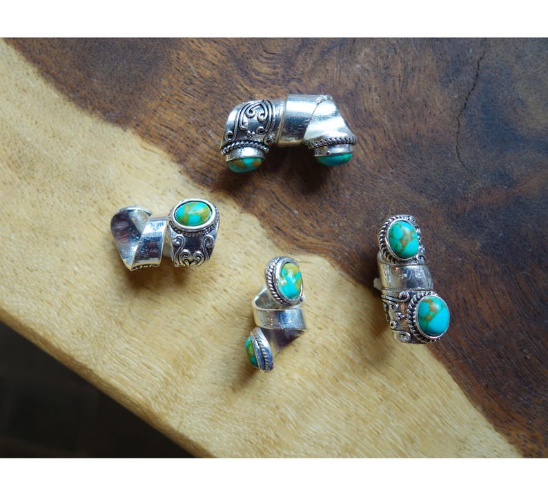 May include: Four silver rings with turquoise stones. The rings are all different designs, but they all have a similar style. The rings are on a wooden surface.
