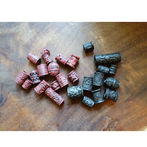 May include: A collection of hair beads in two colors: dark red and black. The beads are cylindrical and have intricate designs carved into their surfaces.