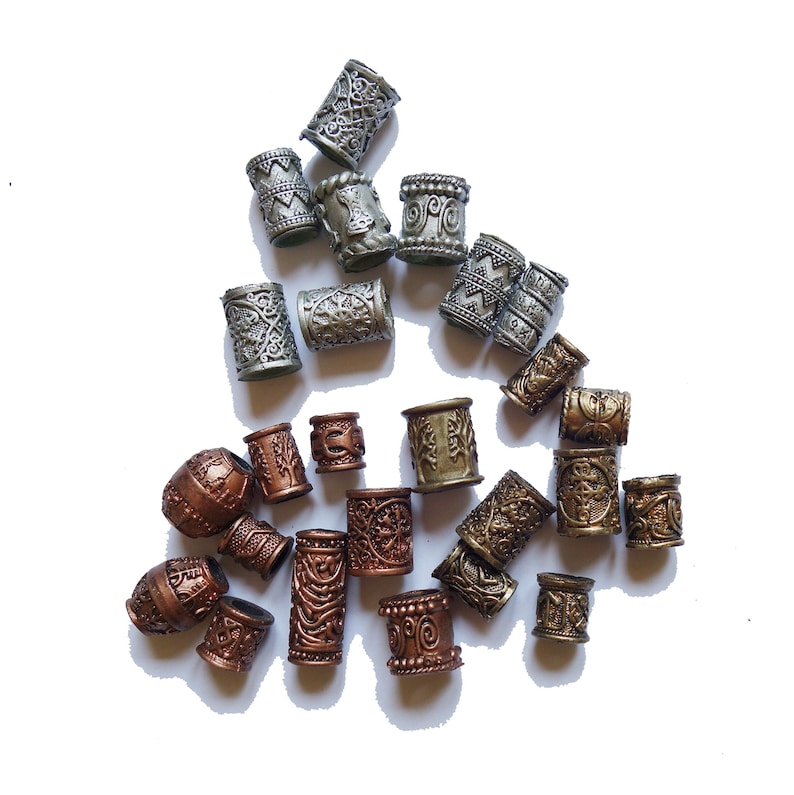 May include: A collection of decorative hair beads in silver, gold, and copper tones. The beads are cylindrical and feature intricate designs.