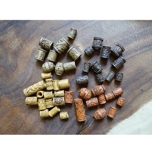 May include: A collection of wooden hair beads with intricate designs. The beads are in three colors: brown, tan, and orange. The beads are arranged in a random pattern on a wooden surface.