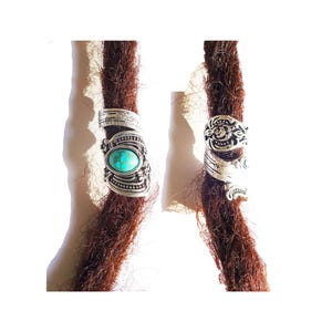 May include: Two silver dreadlock beads with turquoise stones. The beads are ornate and have a floral design.