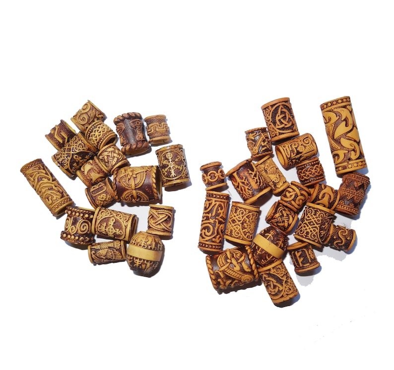May include: A collection of wooden hair beads with intricate carvings. The beads are brown and beige with a variety of patterns, including geometric designs and symbols.