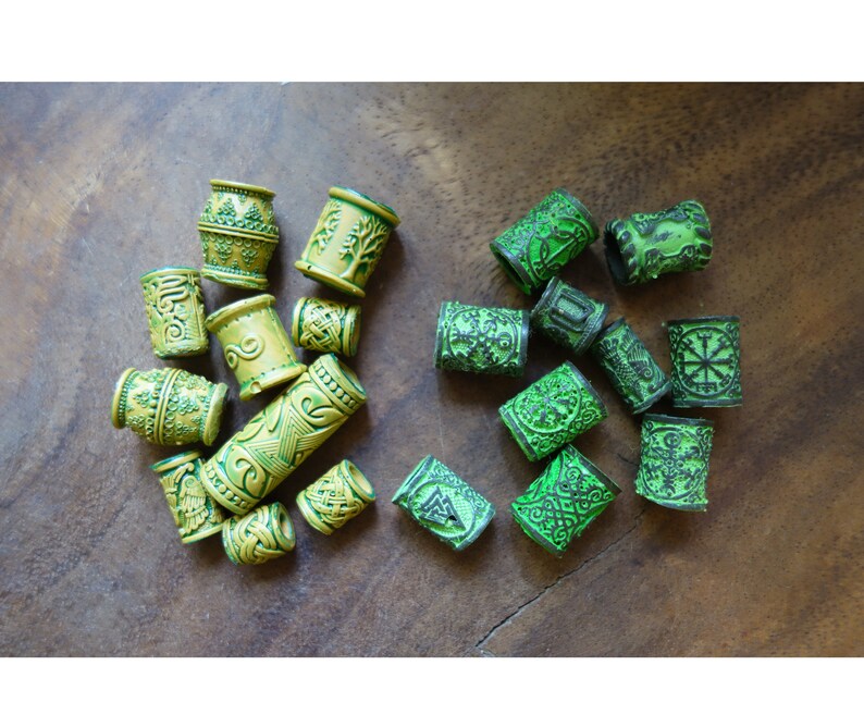 May include: A collection of green and yellow hair beads with intricate designs. The beads are made of plastic and have a glossy finish.