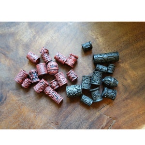 May include: A collection of decorative hair beads in two colors: dark red and black. The beads are cylindrical and have intricate patterns carved into their surfaces.