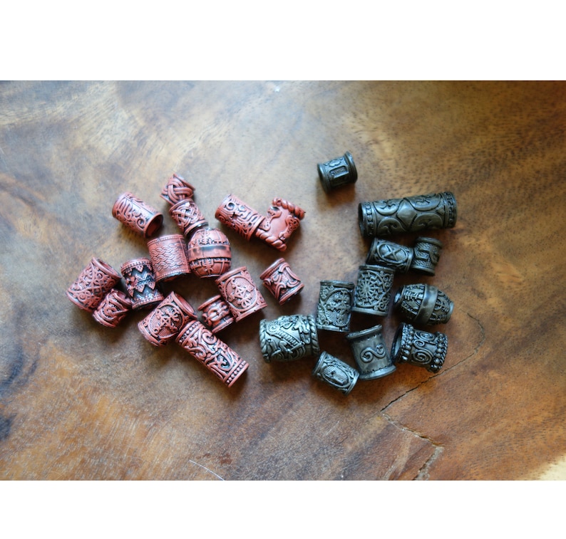 May include: A collection of decorative hair beads in two colors: dark red and black. The beads are cylindrical and have intricate patterns carved into their surfaces.