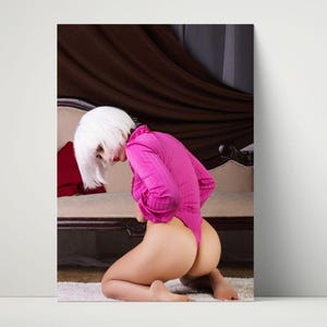 May include: A bright pink bodysuit with long sleeves. The model is kneeling on a white rug in front of a vintage sofa. The person is wearing a white wig.