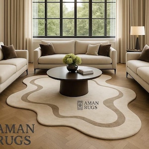 May include: A modern living room with three beige sofas, a dark brown coffee table, and a beige rug with a brown, organic pattern. The room has large windows, beige curtains, and a wooden floor. The rug is from Aman Rugs.