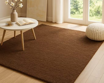 May include: A rectangular brown rug with a textured surface. The rug is placed on a light-coloured wooden floor. A white round table with wooden legs, a vase with flowers, and a pouffe are also in the room.
