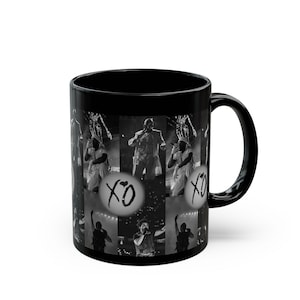 May include: Black ceramic mug featuring a collage of black and white concert photos. The mug includes the text "XO" in a circle. The mug has a black handle and a glossy finish.