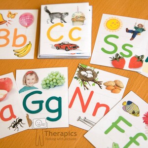 Puede incluir: Un conjunto de tarjetas de memoria del alfabeto con ilustraciones y letras coloridas. Las tarjetas presentan una variedad de im&aacute;genes, incluyendo una campana, un globo, un gato, un coche, un sol, un columpio, un tren, una linterna, una manzana, uvas, un nido de p&aacute;jaro, almendras, un pez y una flor.