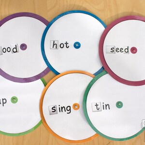 Puede incluir: Seis círculos coloridos con centros blancos y texto negro. Las palabras son "food", "hot", "seed", "tap", "sing" y "tin".