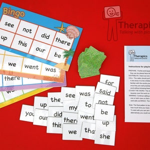 Puede incluir: Un juego de tarjetas de bingo de colores con palabras como "ver", "no", "hizo", "allí", "arriba", "esto", "nuestro", "ser", "a", "nosotros", "fuimos", "fue", "para", y "allí". También hay pequeñas tarjetas blancas con palabras en ellas, como "para", "dijo", "ver", "fue", "el", "no", "a", "arriba", "mi", "ser", "tú", "hizo", "fuimos", "nuestro", "esto", "allí", "nosotros", "eso", y "ella". Las tarjetas están sobre una superficie roja.