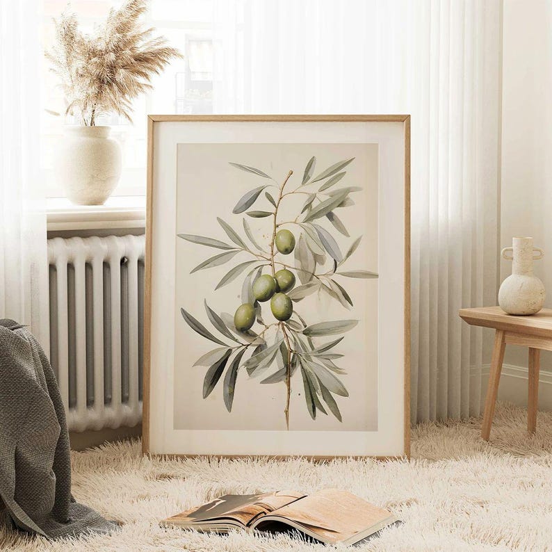May include: A framed botanical print featuring an olive branch with green olives and gray-green leaves. The artwork is set against a cream-colored background and framed in a light wood frame. The print is displayed on a fluffy white rug.