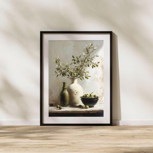Può includere: Stampa artistica incorniciata con una natura morta. Raffigura un vaso bianco con rami di ulivo, una bottiglia verde e una ciotola nera piena di olive. L'opera è ambientata su una superficie di legno.