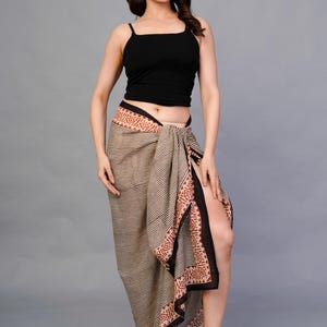 May include: A woman wearing a black camisole top and a wrap skirt. The skirt features a striped pattern with a decorative border in shades of brown and red. The skirt is wrapped around the waist and has a high slit.
