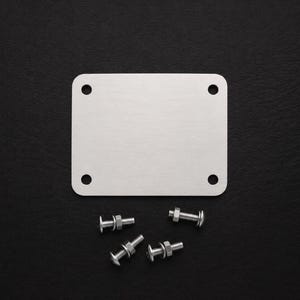 May include: A rectangular silver-colored metal plate with rounded corners and four circular holes, one in each corner. Four small metal bolts with matching nuts and washers are positioned below the plate on a dark surface.