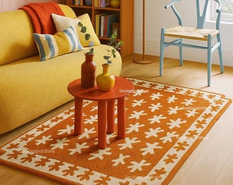May include: A cozy living room scene featuring a yellow sofa, orange rug, and a small round table. The rug has a repeating white floral pattern on an orange background. Decorative pillows and a wooden bookshelf add to the room's inviting atmosphere.