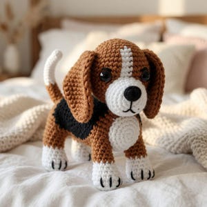 May include: A crocheted beagle dog toy featuring brown, black, and white yarn. The plush figure has long floppy ears, a white muzzle with a black nose, a white chest, and white paws. The tail is upright, and the eyes are made of black plastic beads.