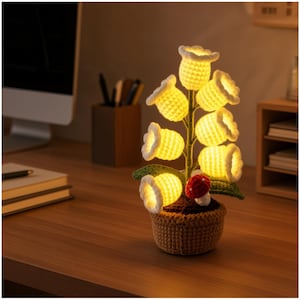 May include: A crochet potted plant lamp featuring seven glowing yellow bell-shaped flowers with white edges, a green stem and leaves, and a small red and white mushroom at the base, all housed in a textured brown crocheted pot.